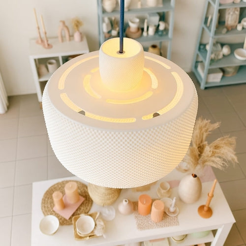 Close-up of a textured pendant light with a blurred background of decorative items on a shelf.