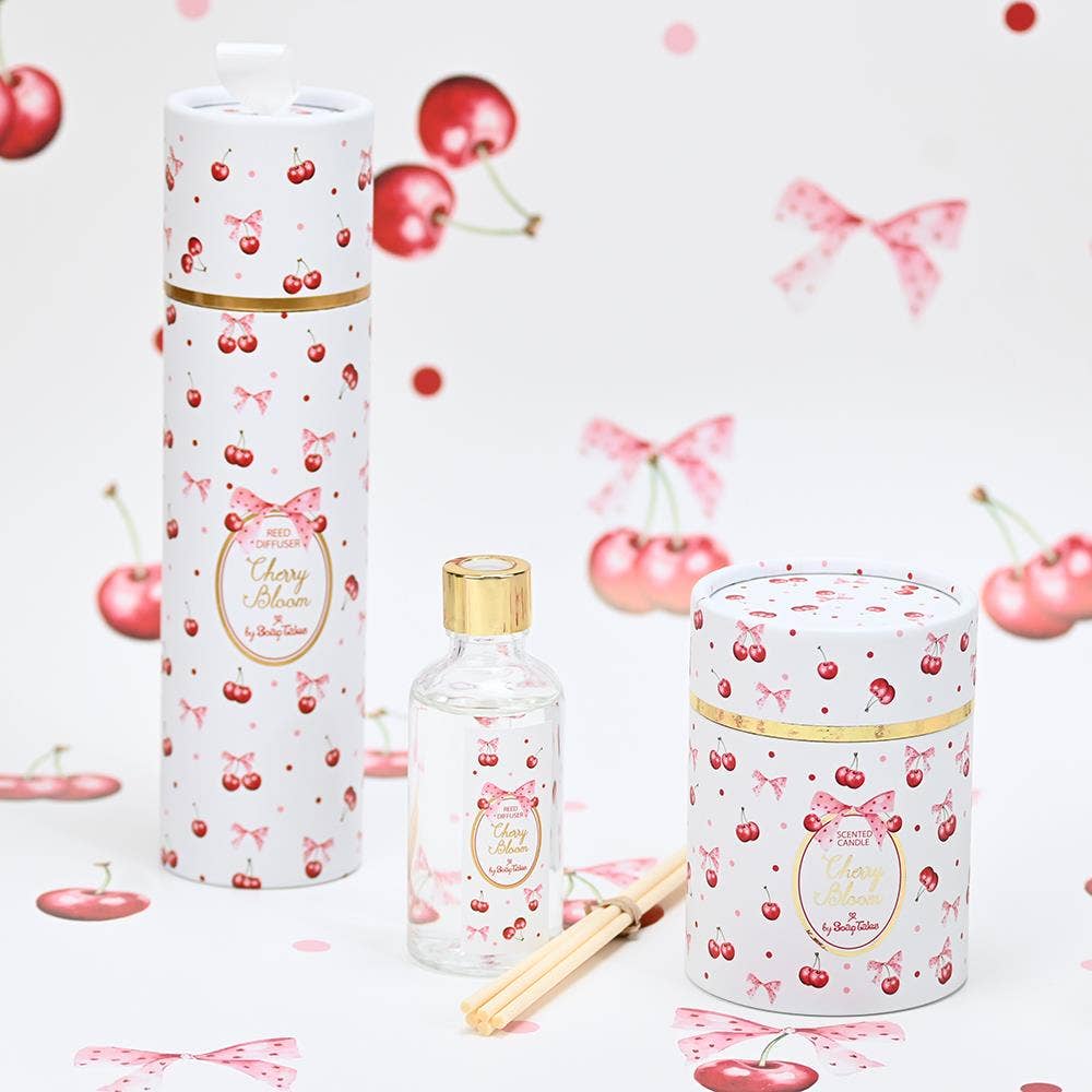 Set of cherry-themed products including a diffuser and candle on a cherry and bow patterned background.