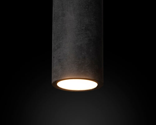 Cylindrical concrete light fixture with a glowing interior on a black background