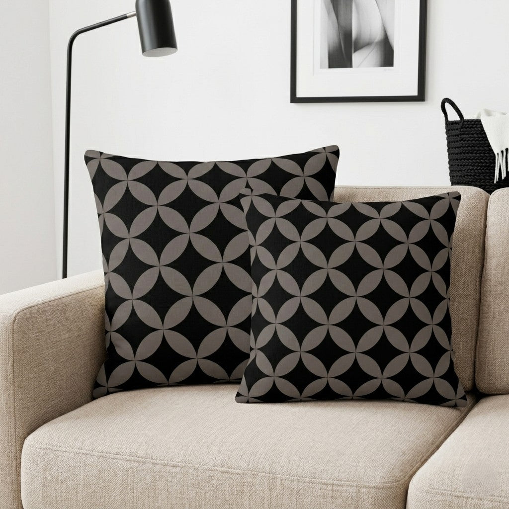 Two black patterned pillows Espresso from Mid-Century Modern Geometric Collection by Lume Vivendi in sizes 18" x 18" and 22" x 22" on a beige sofa with a lamp and abstract art in the background.