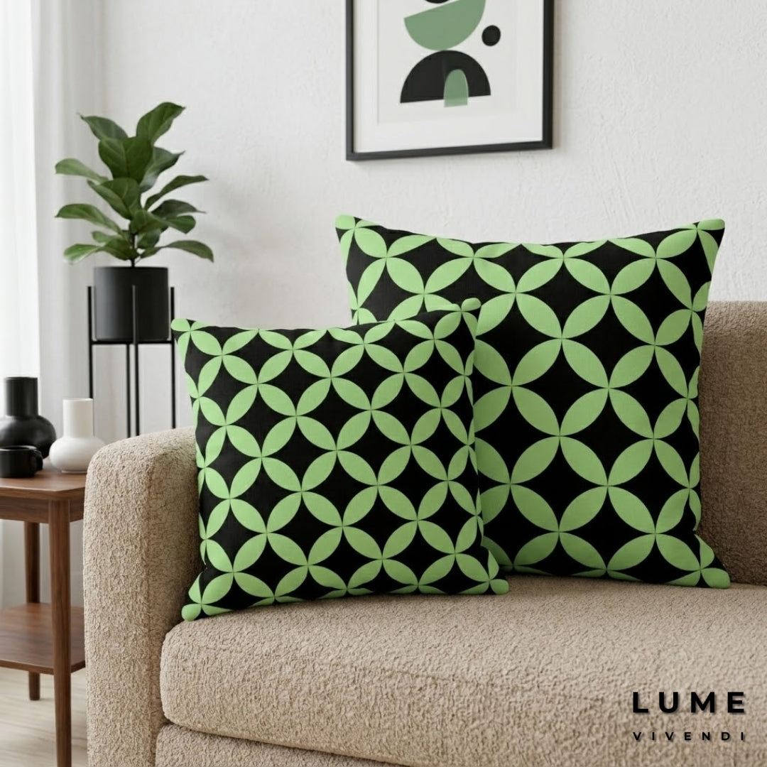 Green and black patterned pillows on a beige sofa with a plant and framed art in the background.