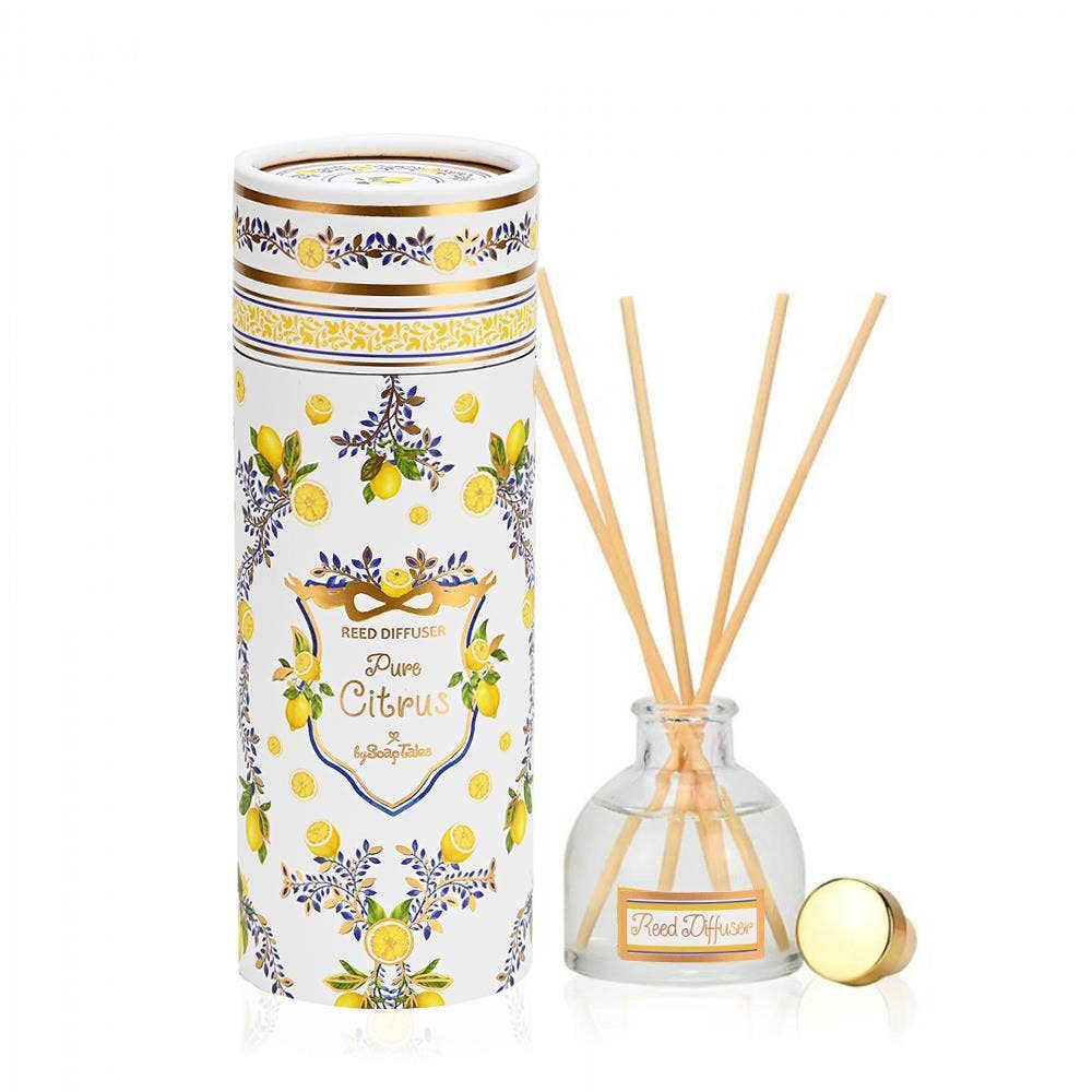 A Pure Citrus reed diffuser by SoapTales featuring a cylindrical gift tube with floral and citrus illustrations in blue and gold, set next to a glass diffuser bottle with wooden reeds.