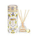 A Pure Citrus reed diffuser by SoapTales featuring a cylindrical gift tube with floral and citrus illustrations in blue and gold, set next to a glass diffuser bottle with wooden reeds.