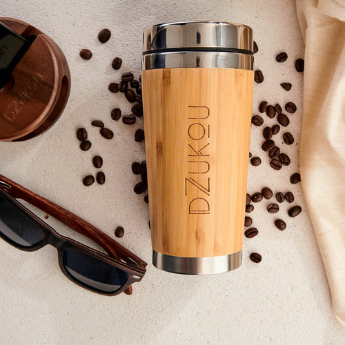 Wooden travel mug with metal lid on a surface with coffee beans and sunglasses.